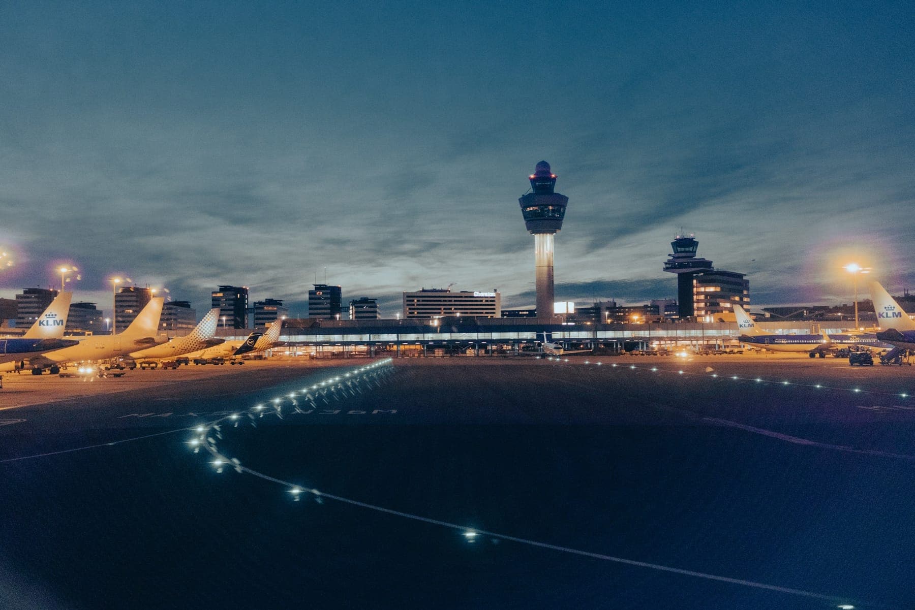 Pátio de aeroporto iluminado à noite, com torre de controle